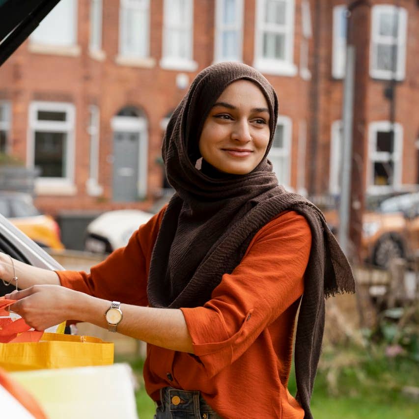 Woman wearing hijab putting shopping bags into car trunk
